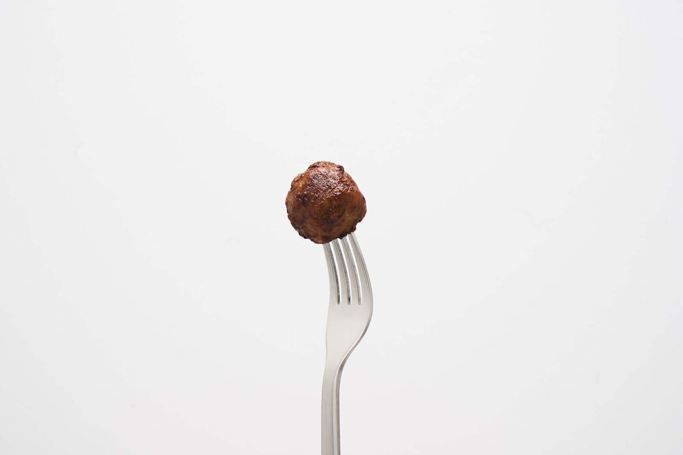 A meatball on a fork against a white background.