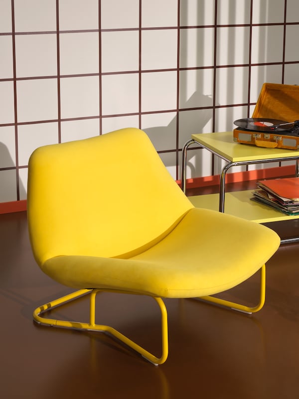 A yellow SOTENÄS armchair stands on a brown floor beside a yellow BAGGBODA side table with a record player and records.