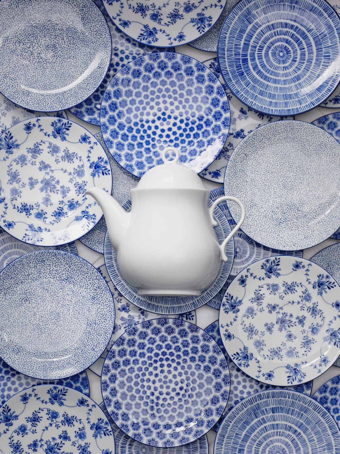 Collection of blue and white patterned ENTUSIASM side plates are spread out, with a white porcelain teapot in the centre.